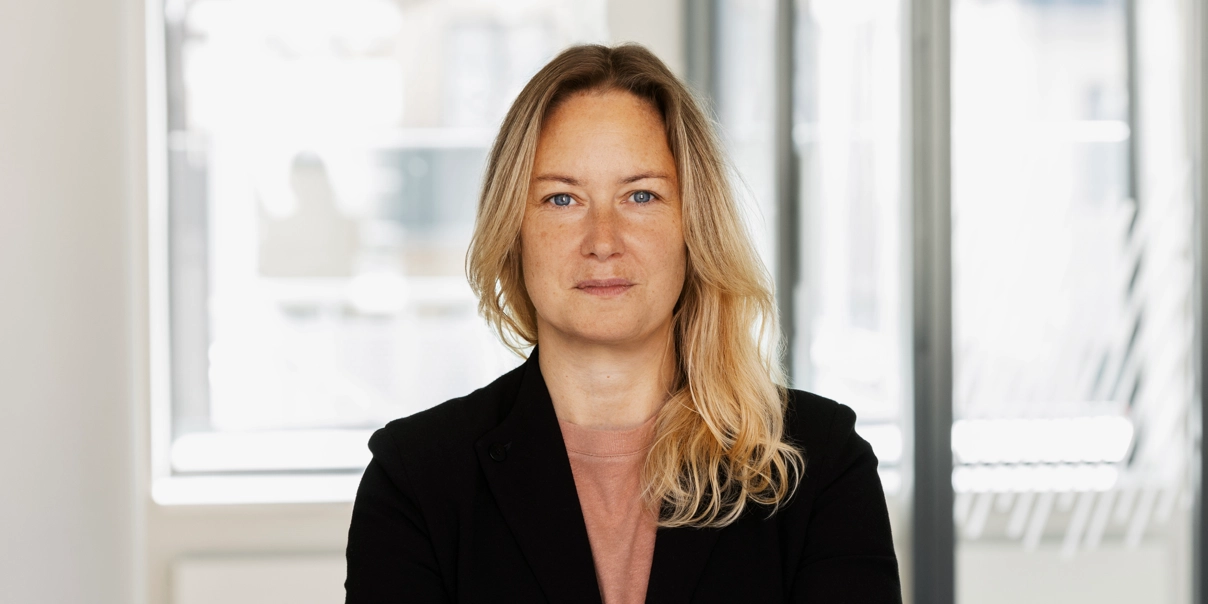 Kvinna med blont halvl&aring;ngt h&aring;r, svart kavaj.