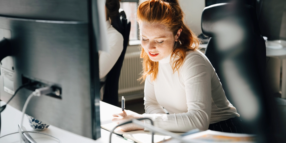 Kvinna vid skrivbord, skriver för hand på papper.