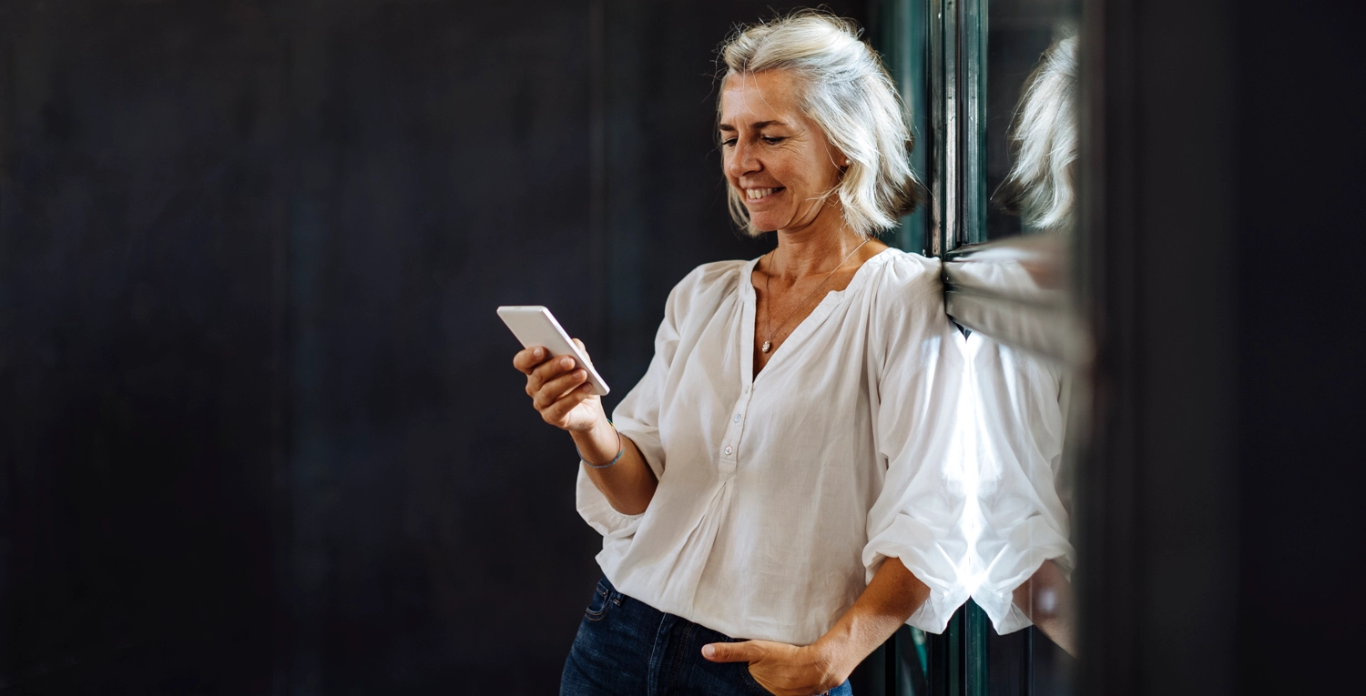 Kvinna lutar sig mot vägg, mobil i handen. framtid arbetsliv ekonom