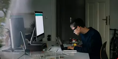 Ung kille sitter fokuserad vid ett skrivbord i hemmamiljö medan han skriver på sin laptop