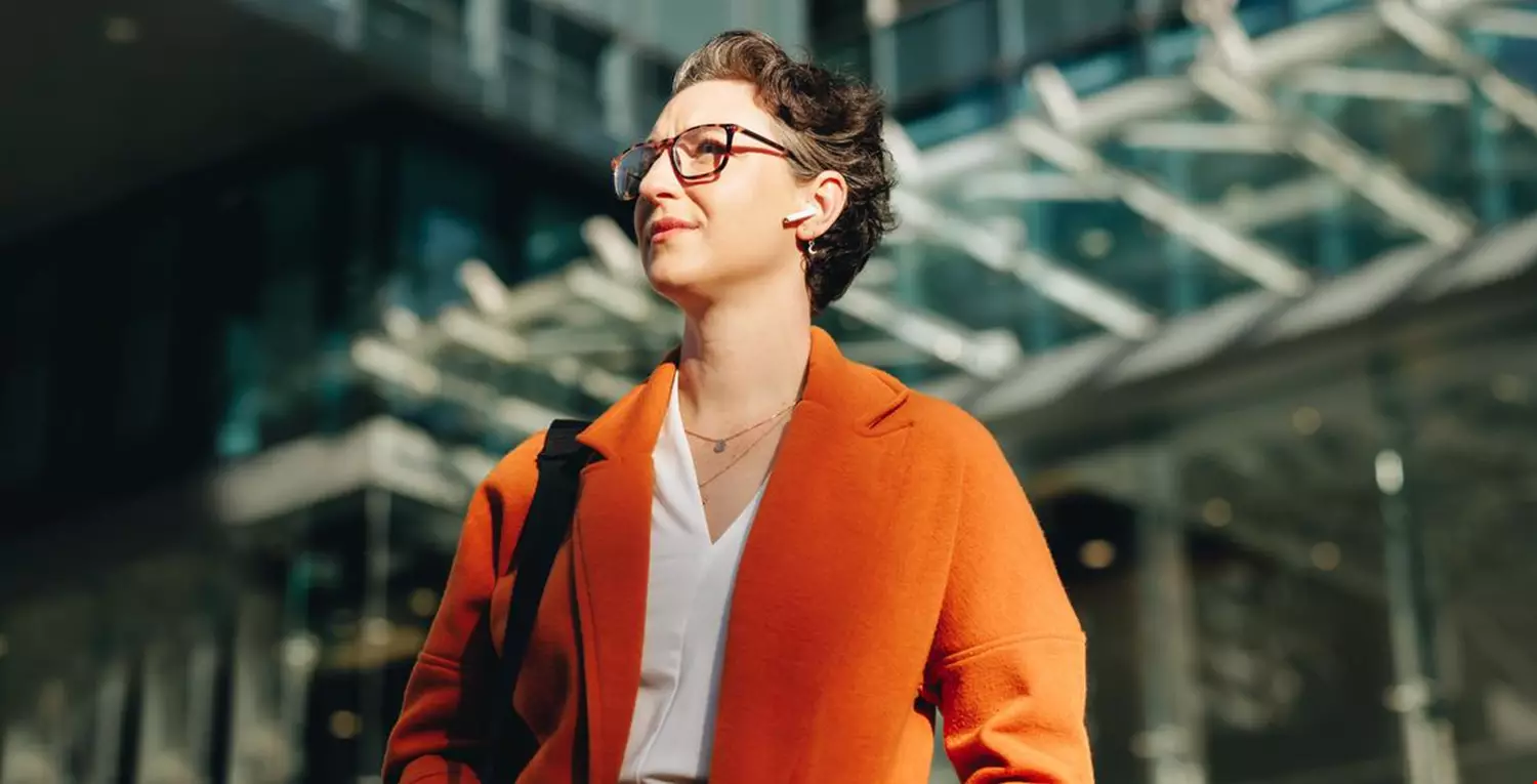 Low angle view of a mature businesswoman listening to music on earphones while commuting to work in the city. Thoughtful businesswoman walking to her office in the morning.