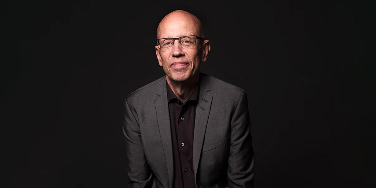 Portr&auml;tt av man i medel&aring;ldern som ler, han har gr&aring; kostym och glas&ouml;gon.