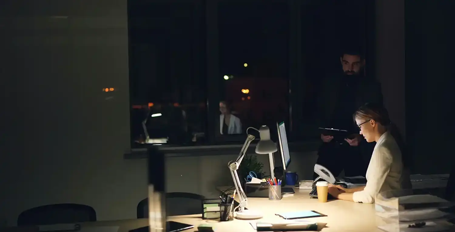 tva kollegor jobbar i en ljuskagla i ett morkt kontor