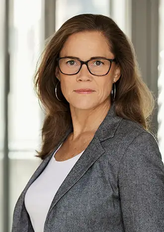 Porträttbild på kvinna med grå kavaj, långt mörkt hår och glasögon.